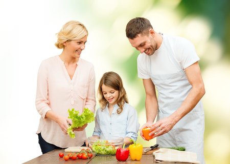 vegetarian food, culinary, happiness and people concept - happy family cooking vegetable salad for dinner green natural backgroundの写真素材