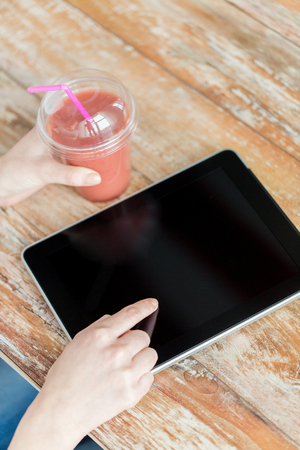 healthy eating, diet, technology and people concept - close up of woman hands with cup of smoothie pointing finger to tablet pc computer black blank screen on wooden tableの写真素材