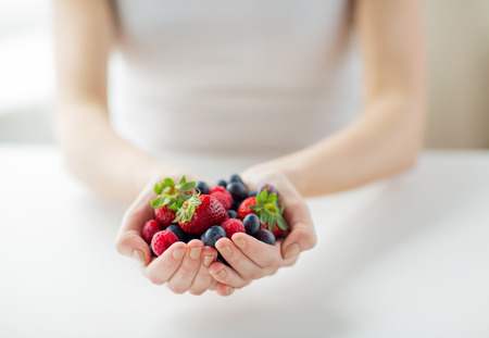 healthy eating, dieting, vegetarian food and people concept - close up of woman hands holding berries at homeの写真素材