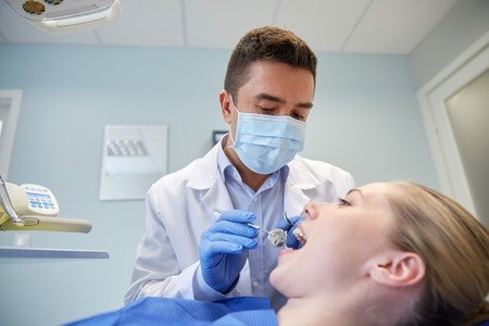 people, medicine, stomatology and health care concept - male dentist in mask with dental mirror and...