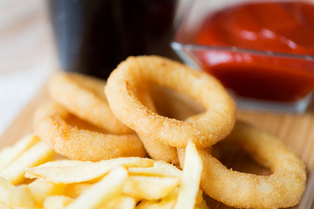 fast food and unhealthy eating concept - close up of deep-fried squid rings, french fries, coca cola...