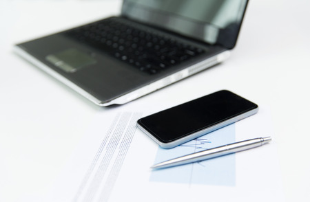 business, technology and statistics concept - close up of smartphone, laptop computer and chart with...