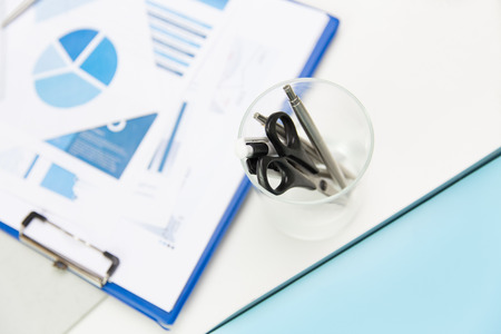 business, stationery and office supply concept - close up of organizer with scissors and pens over charts on tableの写真素材