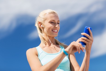 fitness, sport, people, technology and healthy lifestyle concept - smiling young woman with smartphone and earphones listening to music and exercising outdoorsの写真素材