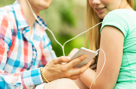 summer vacation, technology and people concept - close up of smiling couple with smartphone and earphones listening to music in parkの写真素材