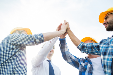 business, building, partnership, gesture and people concept - close up of smiling builders in hardhats making high five outdoorsの写真素材