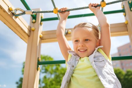 summer, childhood, leisure and people concept - happy little girl on children playground climbing...