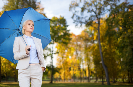 business, season, weather and people and concept - young smiling businesswoman with umbrella over autumn natural backgroundの写真素材