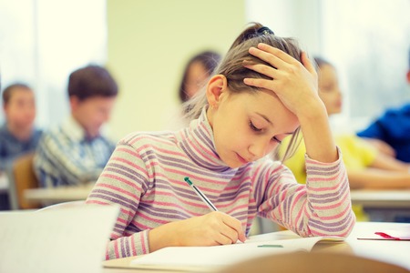 education, elementary school, learning and people concept - group of school kids with pens and notebooks writing test in classroomの写真素材