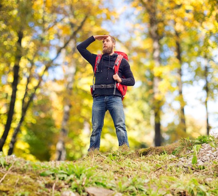 travel, tourism, hike and people concept - tourist with beard, backpack standing on edge of hill and...