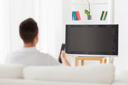 man watching tv and changing channels at home from backの写真素材