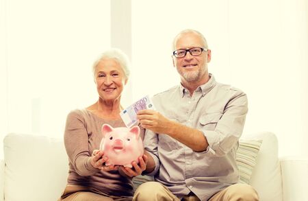 family, savings, age and people concept - smiling senior couple with money and piggy bank at home