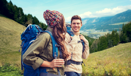 adventure, travel, tourism, hike and people concept - smiling couple walking with backpacks over alpine hills backgroundの写真素材