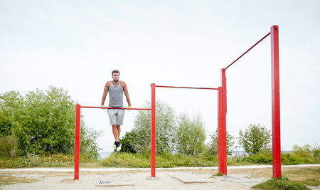 fitness, sport, training and lifestyle concept - young man exercising on horizontal bar outdoors