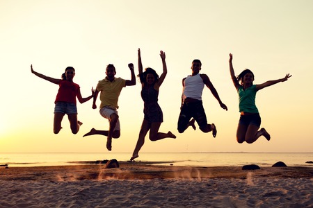 friendship, summer vacation, holidays, party and people concept - group of smiling friends dancing and jumping on beachの写真素材