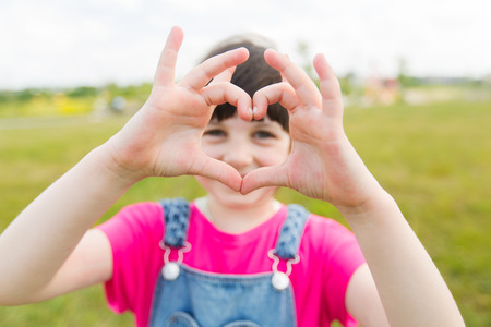 summer, childhood, leisure, love and people concept - happy little girl making heart shape gesture...