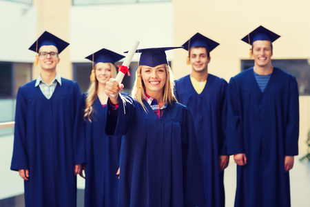 education, graduation and people concept - group of smiling students in mortarboards and gowns with diploma outdoorsの写真素材