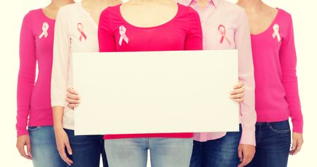 healthcare, people and medicine concept - close up of women in shirts with pink breast cancer awareness ribbons and blank white board over white backgroundの写真素材