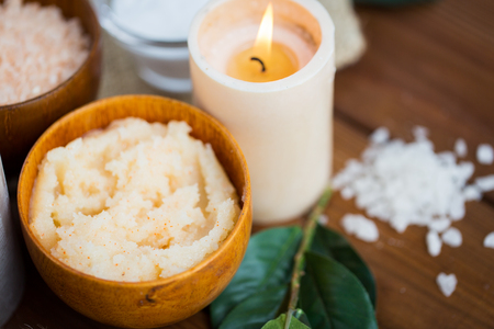 beauty, spa, therapy, natural cosmetics and wellness concept - close up of body scrub and candle on woodの写真素材