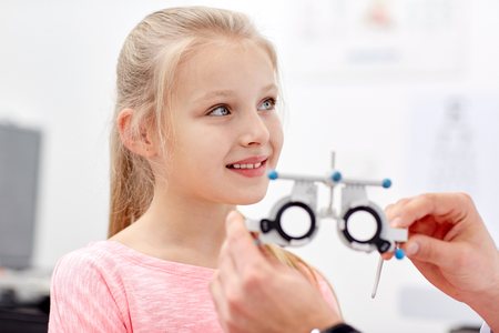 health care, medicine, people, eyesight and technology concept - optometrist with trial frame checking girl patient vision at eye clinic or optics storeの写真素材