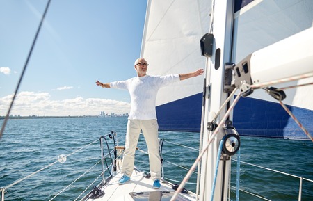 sailing, age, tourism, travel and people concept - happy senior man enjoying freedom on sail boat or yacht floating in seaの写真素材