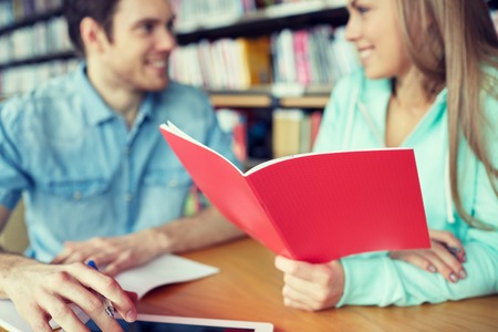 people, learning, communication, education and school concept - close up of happy students with notebooks talking in libraryの写真素材