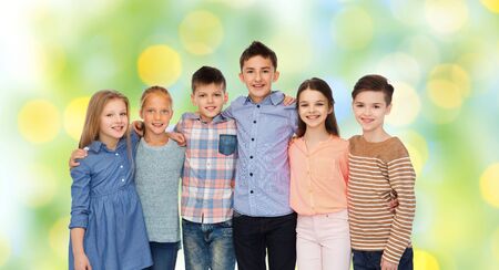 childhood, fashion, friendship and people concept - happy smiling children hugging over green lights...