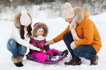 parenthood, fashion, season and people concept - happy family with child on sled walking in winter forestの写真素材