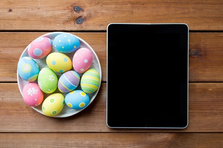 easter, holidays, technology, advertisement and object concept - close up of colored easter eggs on plate and blank tablet pc computerの写真素材