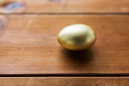 easter, holidays, tradition and object concept - close up of golden easter egg on woodの写真素材