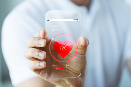 business, technology, health care and people concept - close up of male hand holding and showing transparent smartphone with heart rate iconの写真素材