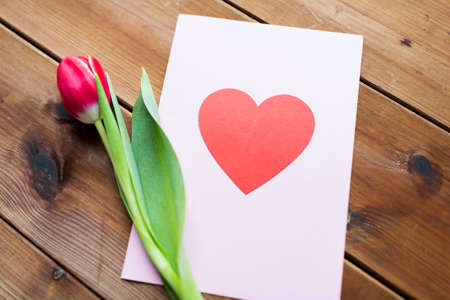 holidays, love and valentines day concept - close up of tulip flowers and greeting card with heart on wooden tableの写真素材