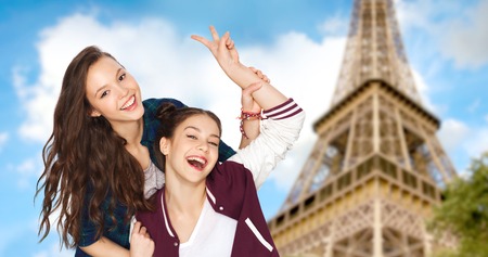 people, travel, tourism and friendship concept concept - happy smiling pretty teenage girls showing peace hand sign over eiffel tower in paris backgroundの写真素材