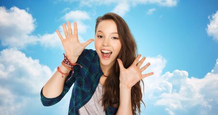 people and teens concept - happy laughing pretty teenage girl showing hands over blue sky and clouds backgroundの写真素材