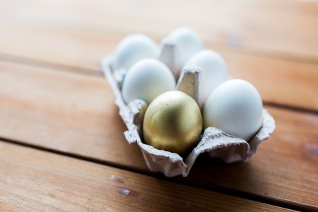 easter, food, cooking and object concept - close up of white and golden eggs in egg box or carton wooden surfaceの写真素材