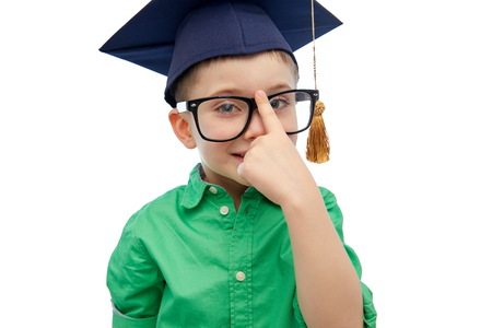 childhood, school, education, knowledge and people concept - happy boy in bachelor hat or mortarboard and eyeglassesの写真素材
