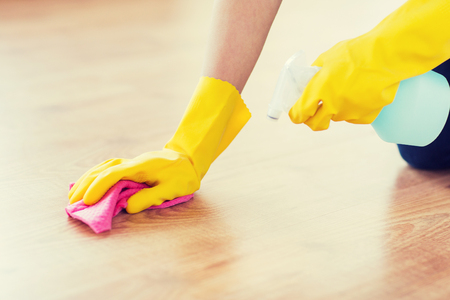 people, housework and housekeeping concept - close up of woman in rubber glover with cloth and detergent spray cleaning floor at homeの写真素材