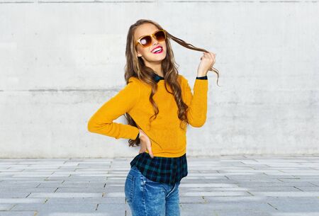 people, style and fashion concept - happy young woman or teen girl in casual clothes and sunglasses over urban street backgroundの写真素材