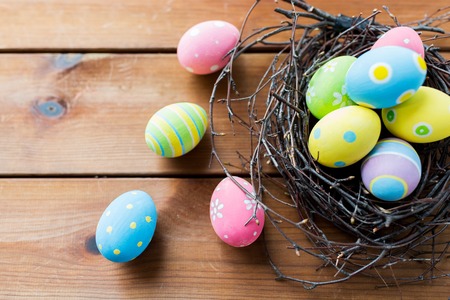 easter, holidays, tradition and object concept - close up of colored easter eggs in nest on wooden surfaceの写真素材