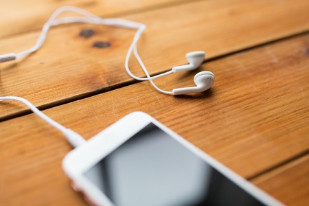 technology, music, gadget and object concept - close up of white smartphone and earphones on wooden surfaceの写真素材