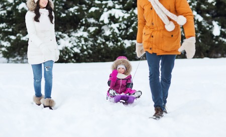 parenthood, fashion, season and people concept - happy family with child on sled walking in winter...