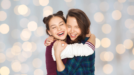 people, friends, teens and friendship concept - happy smiling pretty teenage girls hugging and laughing over holidays lights backgroundの写真素材