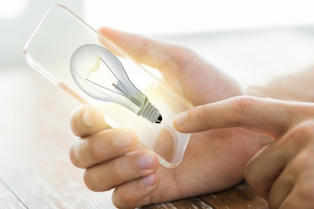technology, startup, idea and business concept - close up of male hand holding transparent smartphone with light bulb on screenの写真素材
