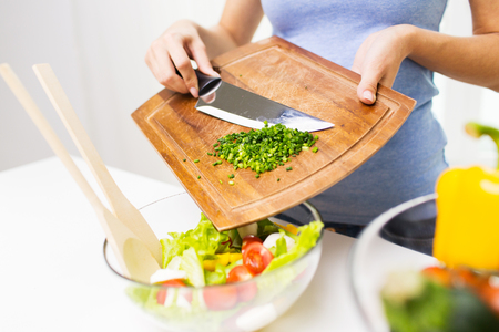 healthy eating, cooking, vegetarian food, diet and people concept - close up of woman adding chopped green onion to saladの写真素材