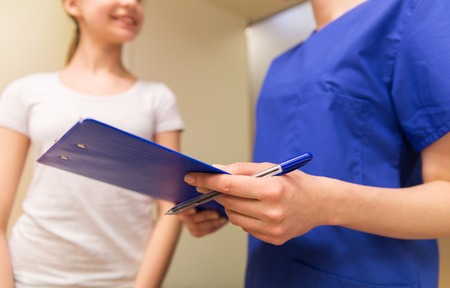 medicine, health care and people concept - close up of female doctor or nurse holding clipboard with pen and talking to girl at hospitalの写真素材