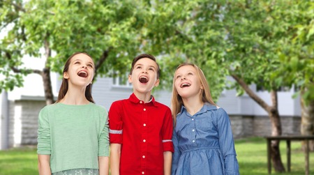 childhood, fashion, friendship and people concept - happy amazed boy and girls looking up with open mouths over private house backyard backgroundの写真素材