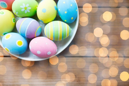 easter, holidays, tradition, advertisement and object concept - close up of colored easter eggs on plate over holidays lightsの写真素材