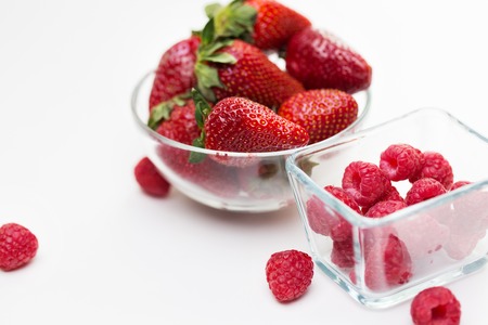 fruits, berries, diet, eco food and objects concept - close up of juicy fresh ripe red strawberries and raspberries in glass bowls over whiteの写真素材