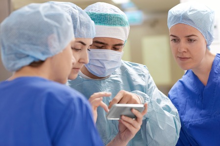 surgery, medicine and people concept - group of surgeons with smartphone in operating room at hospitalの写真素材