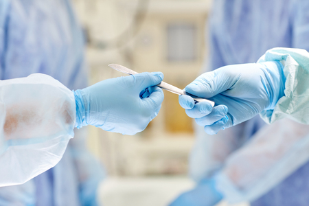 surgery, medicine and people concept - close up of surgeons hands with scalpel at operation in operating room at hospitalの写真素材